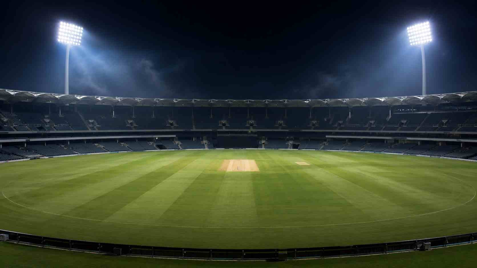 Cricket stadium and illuminated pitch under floodlights at night.